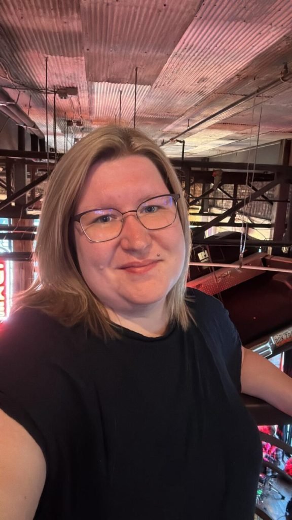 ADA-konforme WordPress-Websites - gebaut für das US-Recht 1 Eine Frau mit blonden Haaren und Brille lächelt in einer Innenraumkulisse in die Kamera.