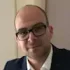 Hombre con gafas y traje de chaqueta oscuro sonríe hacia la cámara.